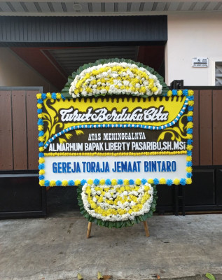 Papan Bunga Duka di Belakang Balok